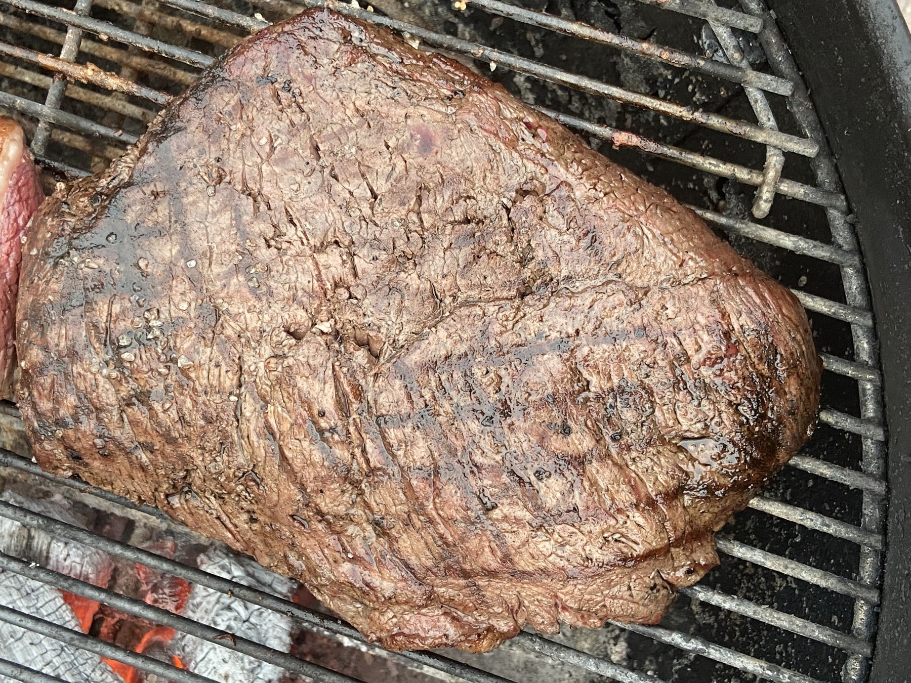 Ganzes Stück Picanha mit grober Salzkruste auf dem Holzkohlegrillrost über der Glut