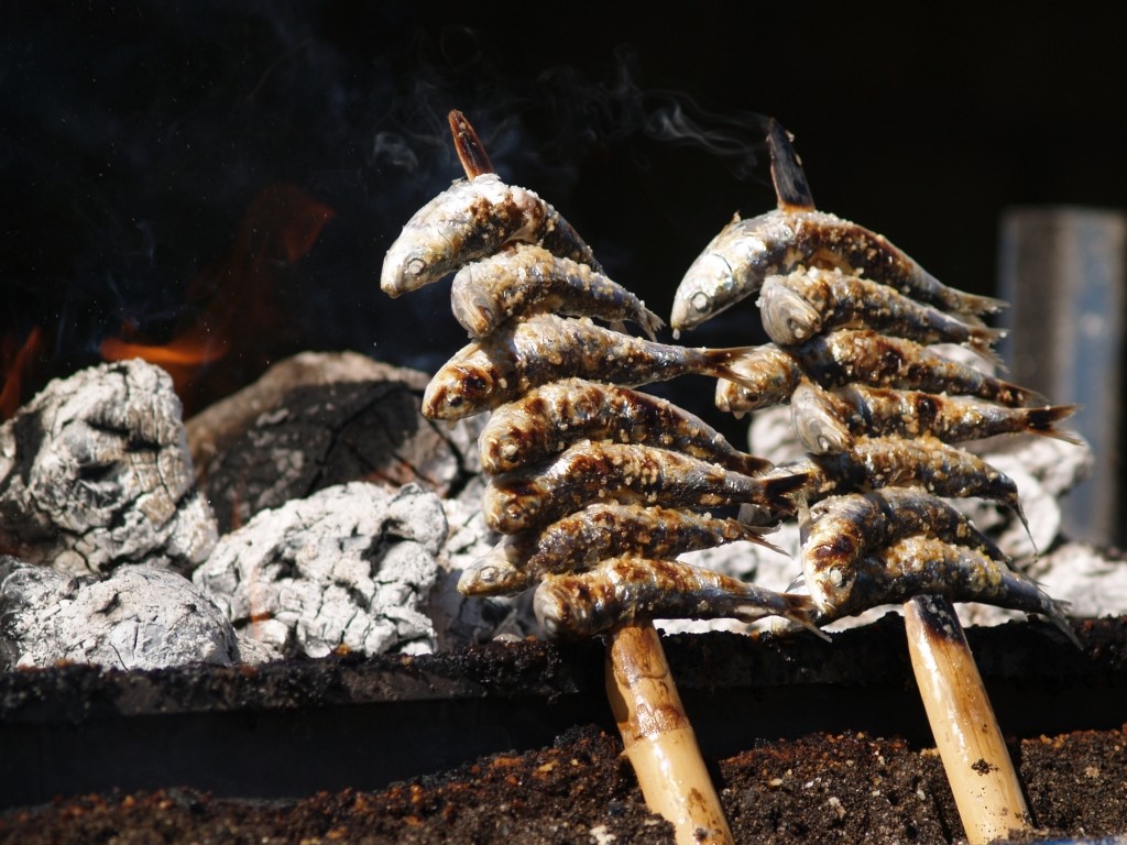 Auf Holzspieße gefädelte Sardinen grillen schräg über offener Glut