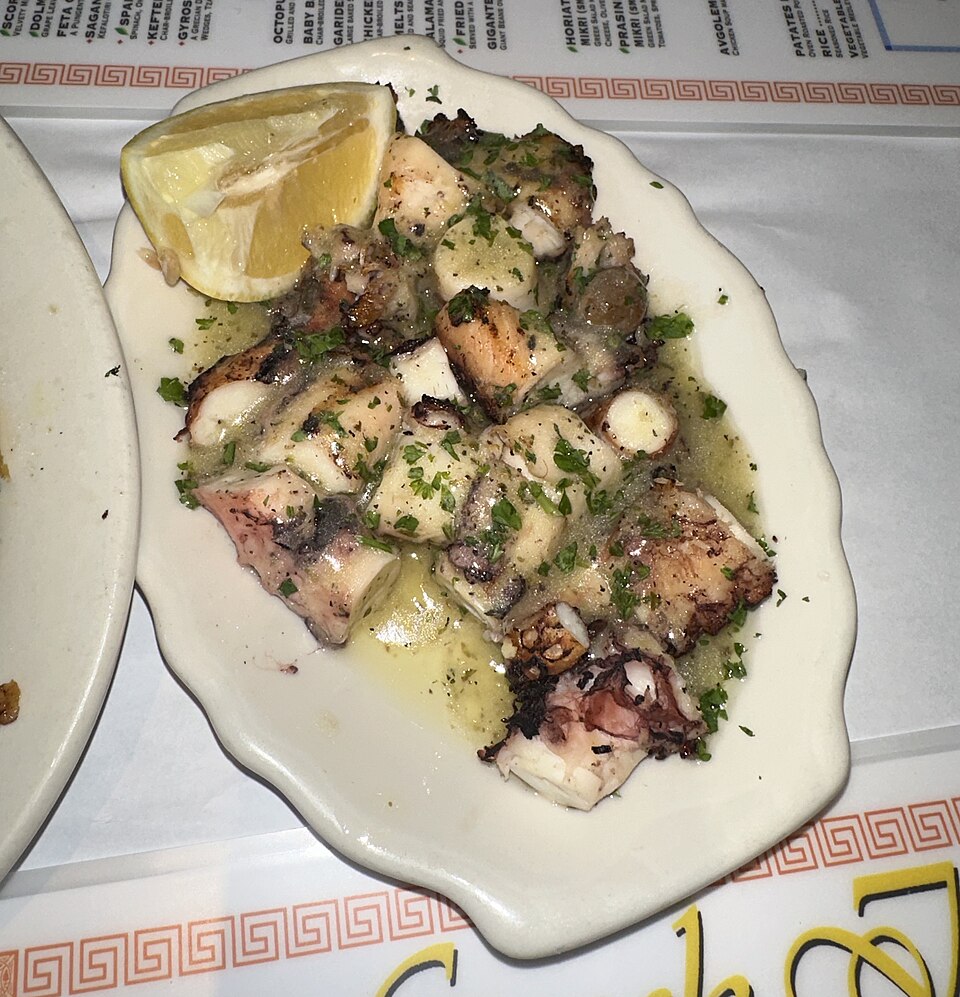 Gegrillte Oktopusstücke mit Zitrone, Olivenöl und Petersilie auf einem Teller
