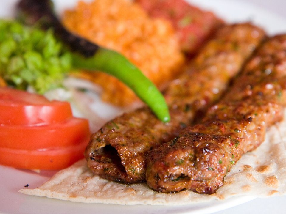 Zwei Adana-Kebap-Spieße auf Fladenbrot mit Tomaten, Salat und grüner Chili