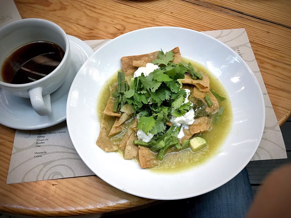 Teller mit Chilaquiles in grüner Salsa mit Koriander, daneben Kaffee