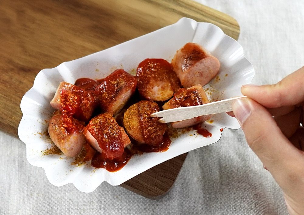 Currywurst mit Sauce und Currypulver in einer Pappschale