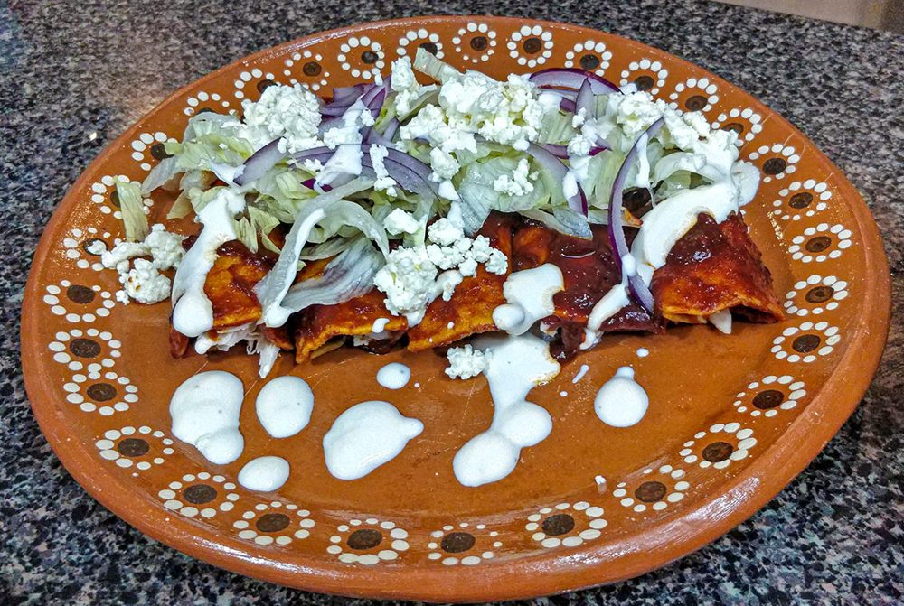 Rote Enchiladas mit Käse, Salat und Crema auf einem Tonteller