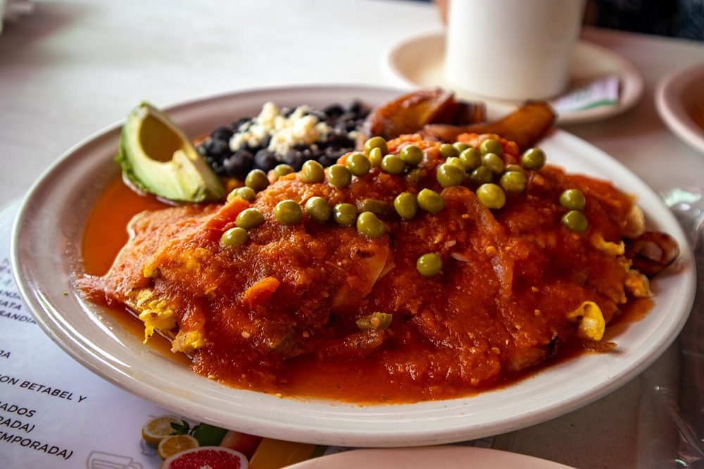 Teller mit Huevos motuleños in Tomatensauce mit Erbsen und Kochbanane