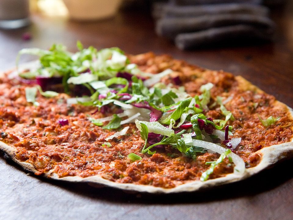 Lahmacun-Fladen mit Hackfleischbelag, garniert mit Salat und roten Zwiebeln