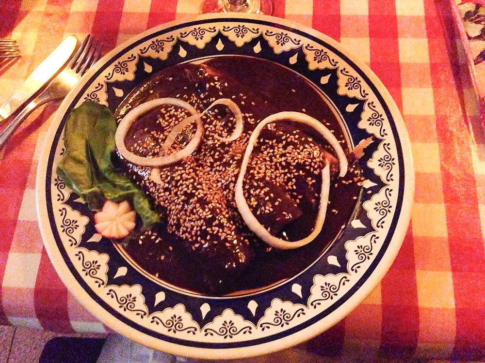 Teller mit dunkler Mole poblano, Sesam und Zwiebelringen